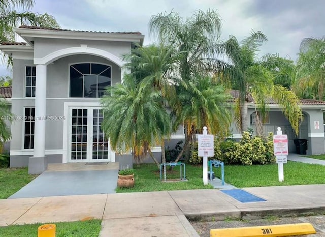 exterior space featuring a tile roof, a front yard, stucco siding, and french doors