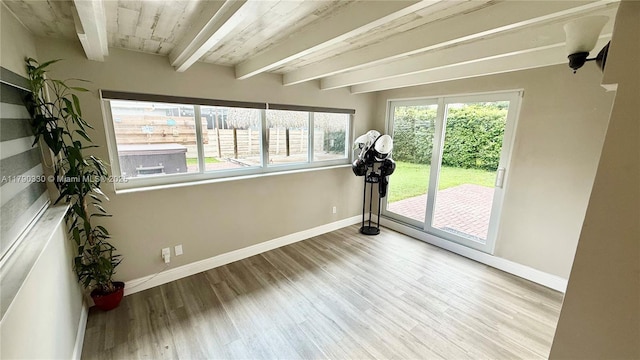 spare room featuring beam ceiling, wood finished floors, and baseboards