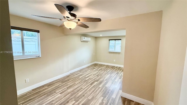 spare room featuring a wall mounted air conditioner, ceiling fan, wood finished floors, and baseboards