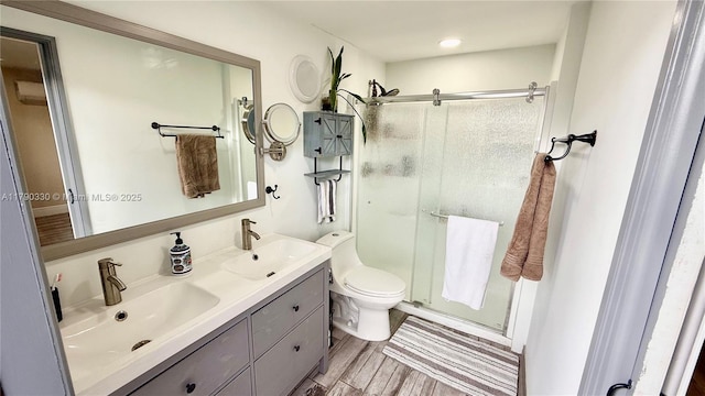 bathroom featuring double vanity, wood finished floors, a stall shower, and a sink