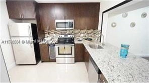 3100 NW 42nd Ave Unit D202, Coconut Creek, FL 33066 - kitchen with a sink, appliances with stainless steel finishes, dark brown cabinetry, a peninsula, and backsplash