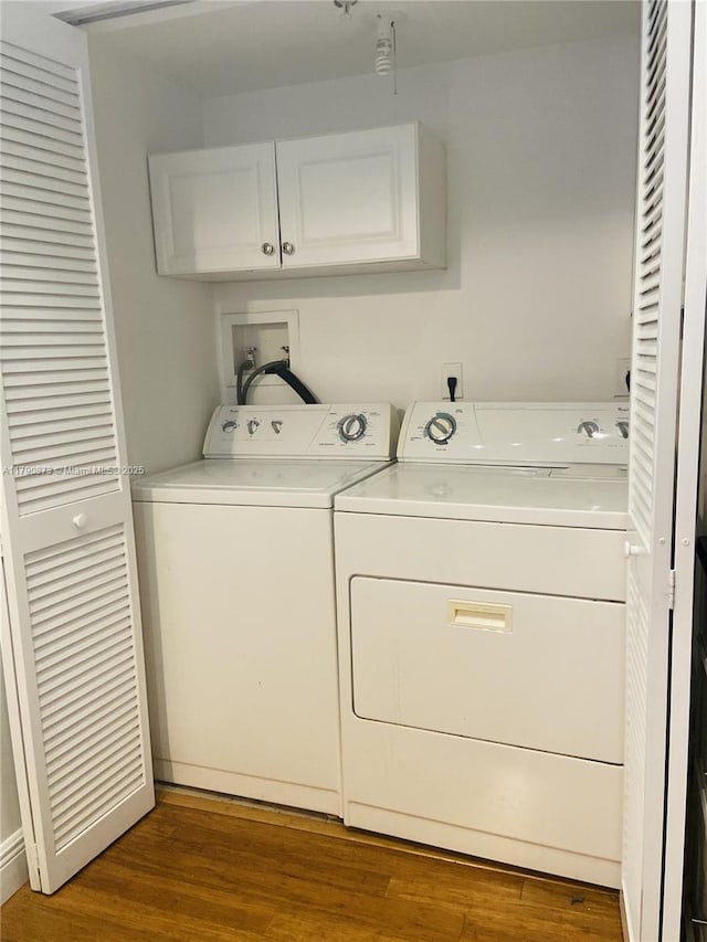 clothes washing area featuring wood finished floors, washer and clothes dryer, and cabinet space