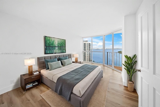 bedroom with light wood-style floors, access to outside, a water view, and expansive windows