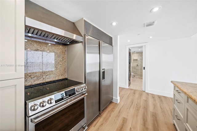 kitchen featuring recessed lighting, decorative backsplash, appliances with stainless steel finishes, light wood-type flooring, and premium range hood