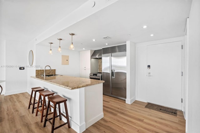 kitchen featuring a sink, stainless steel appliances, a breakfast bar area, a peninsula, and wall chimney range hood