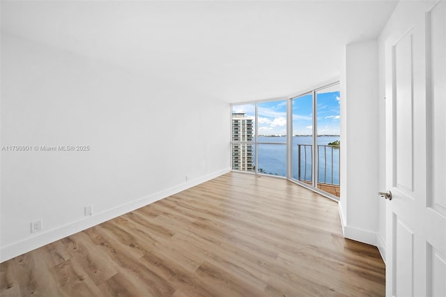 unfurnished room featuring floor to ceiling windows, wood finished floors, a water view, and baseboards