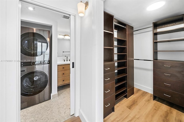 walk in closet with visible vents, stacked washer / dryer, light wood finished floors, and a sink