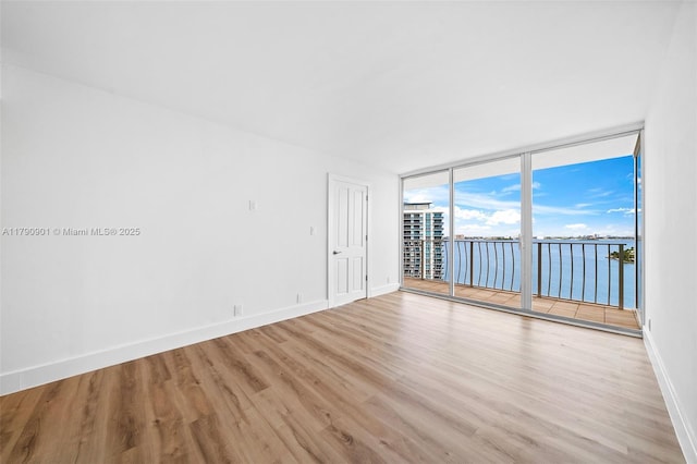 empty room with a water view, baseboards, expansive windows, and light wood-style floors