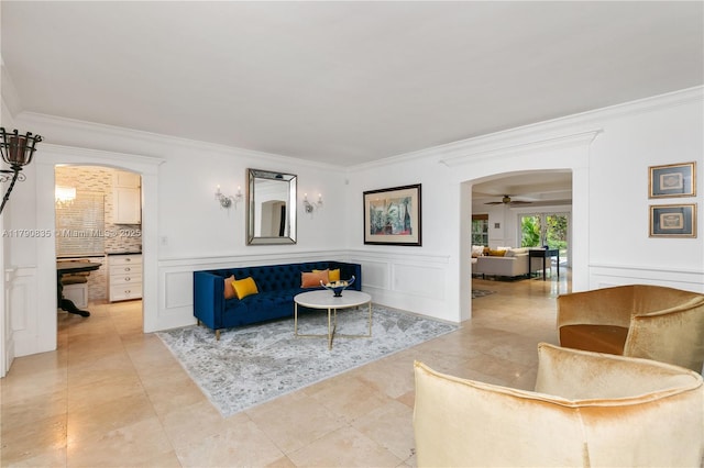living area with crown molding, a ceiling fan, and a decorative wall