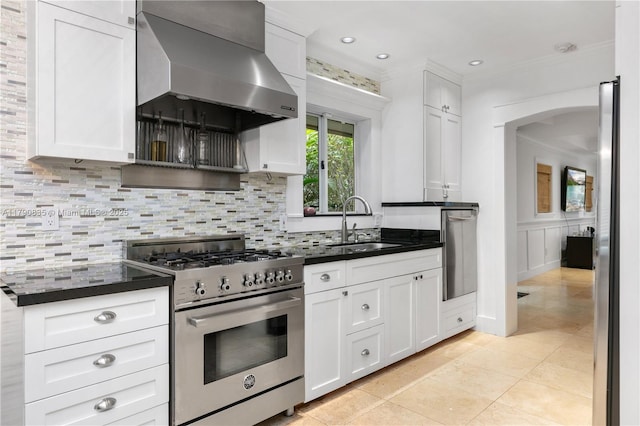 kitchen featuring wall chimney range hood, appliances with stainless steel finishes, dark countertops, and a sink
