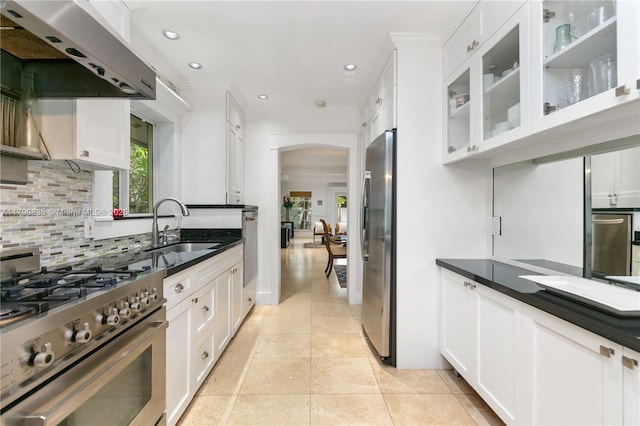 kitchen featuring backsplash, appliances with stainless steel finishes, range hood, arched walkways, and a sink