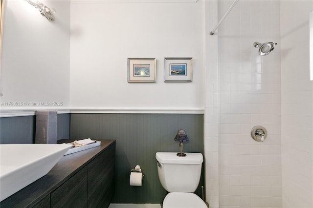 full bath with vanity, a wainscoted wall, a tile shower, and toilet