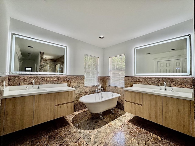 full bath featuring a sink, a soaking tub, two vanities, and tile walls