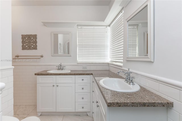 full bathroom with double vanity, tile walls, wainscoting, and a sink