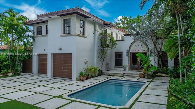 back of property featuring an attached garage, an outdoor pool, stucco siding, and a tile roof