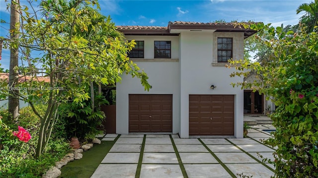 mediterranean / spanish-style house featuring a tiled roof, an attached garage, driveway, and stucco siding