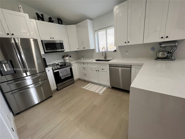 kitchen featuring white cabinetry, a sink, appliances with stainless steel finishes, light wood-style floors, and light countertops