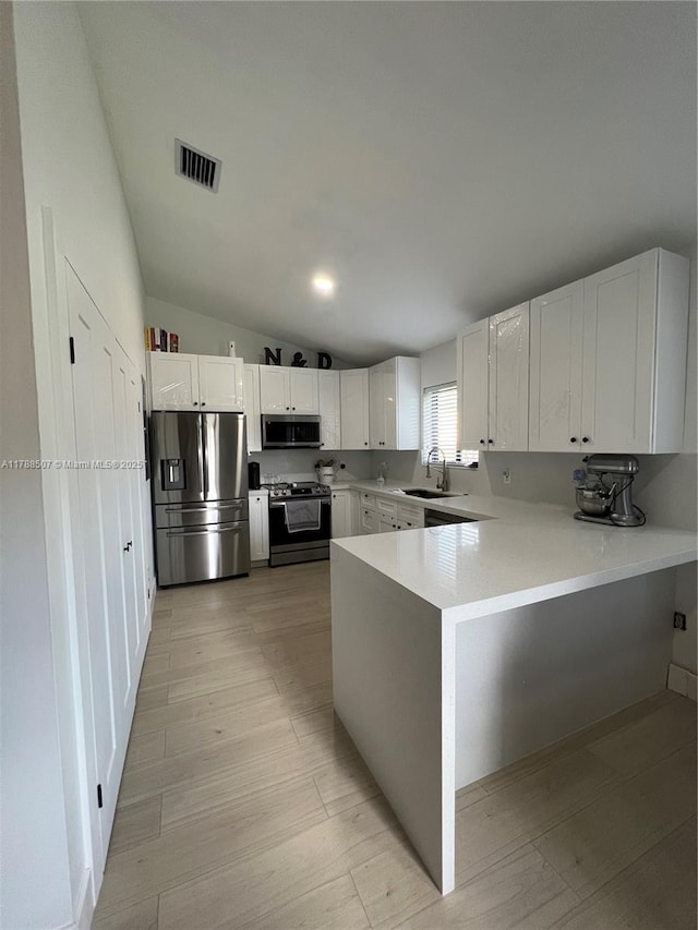 kitchen featuring stainless steel appliances, a sink, visible vents, a peninsula, and lofted ceiling
