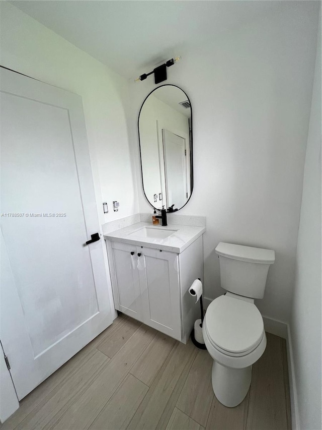 half bathroom with baseboards, wood finished floors, toilet, and vanity