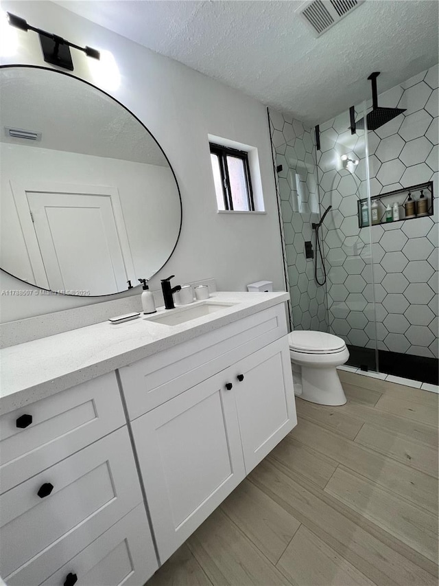 full bathroom with a shower stall, vanity, toilet, visible vents, and a textured ceiling