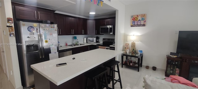 kitchen featuring a sink, stainless steel appliances, a kitchen bar, a kitchen island, and light countertops