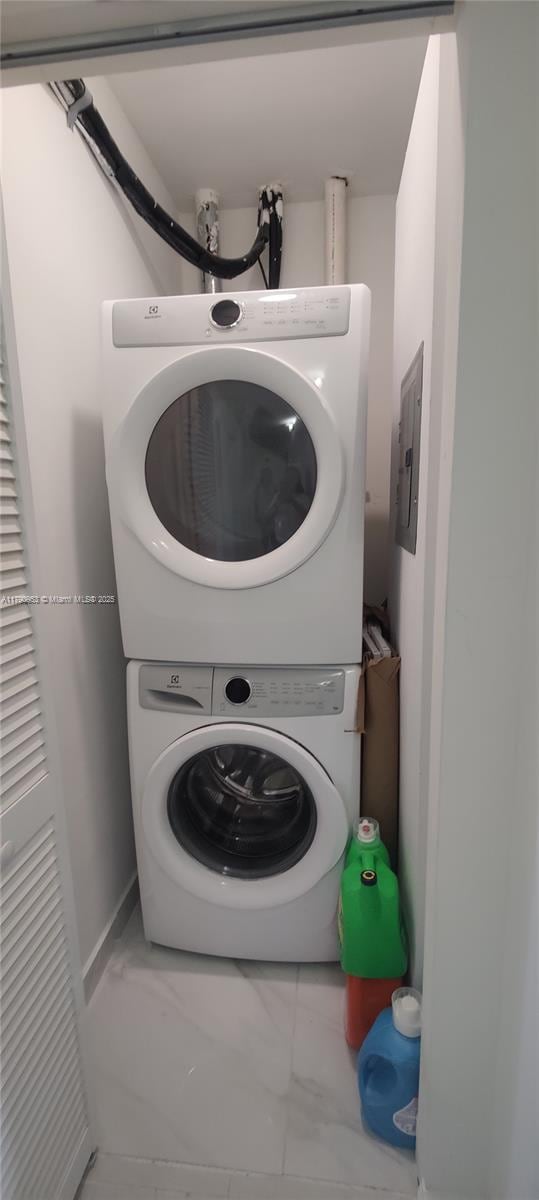 clothes washing area featuring stacked washer / dryer, marble finish floor, electric panel, and laundry area