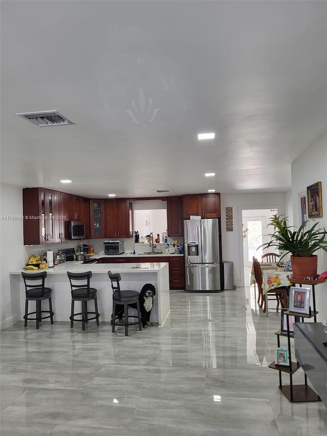 kitchen featuring visible vents, stainless steel appliances, light countertops, a kitchen bar, and a peninsula