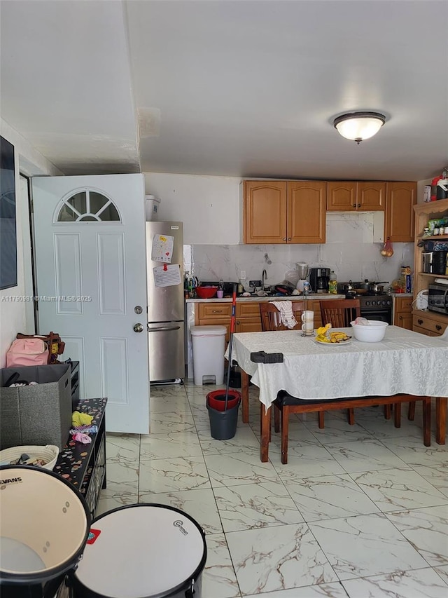kitchen with range with gas stovetop, marble finish floor, freestanding refrigerator, and backsplash
