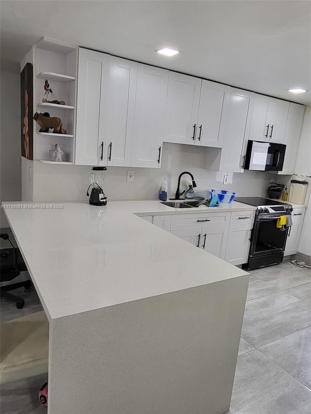 kitchen featuring electric stove, a sink, white cabinetry, black microwave, and a peninsula