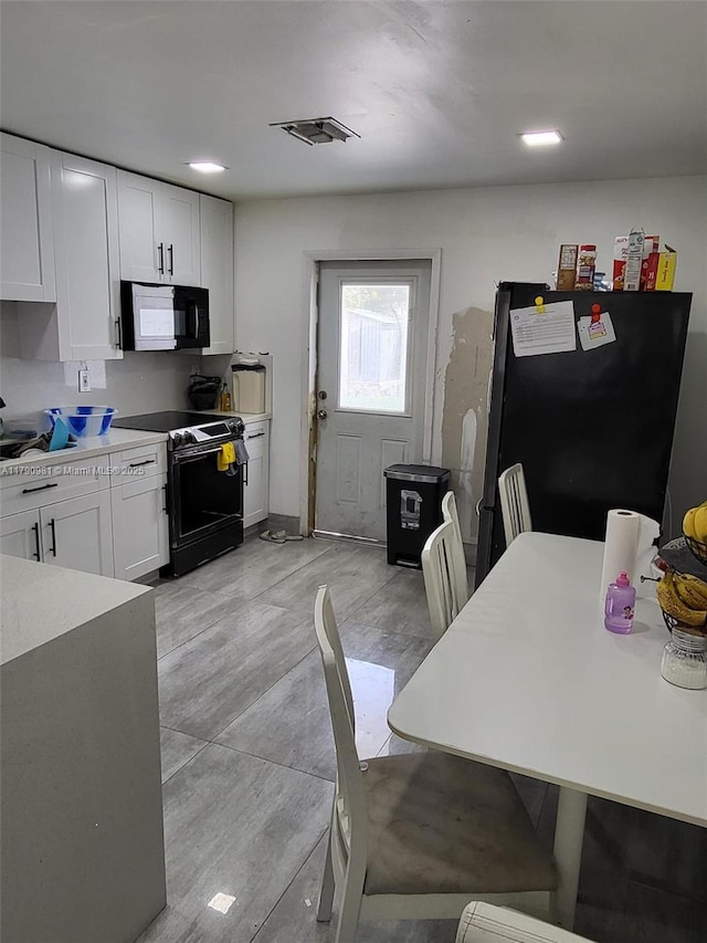 kitchen featuring black range with electric stovetop, white cabinetry, visible vents, light countertops, and freestanding refrigerator