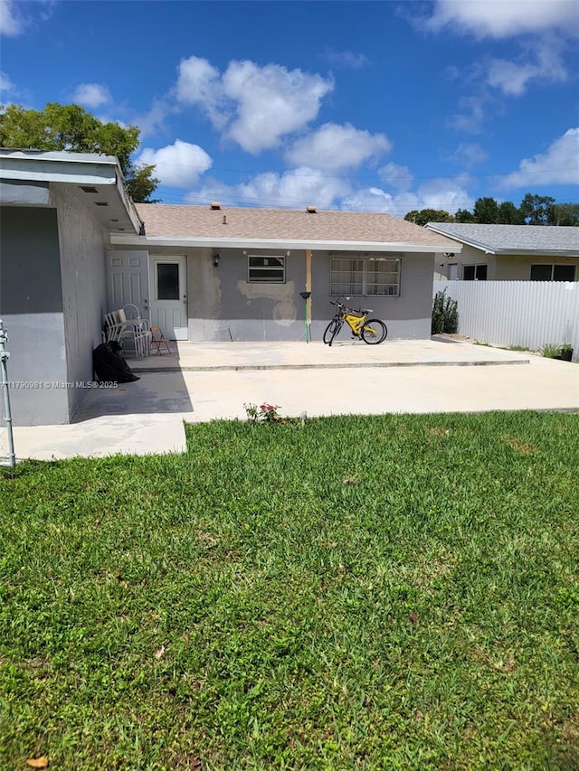 rear view of house with stucco siding, fence, a lawn, and a patio