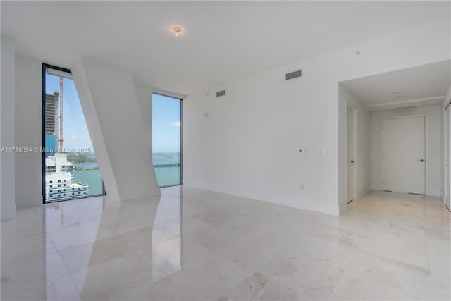 unfurnished room with floor to ceiling windows, visible vents, and a water view