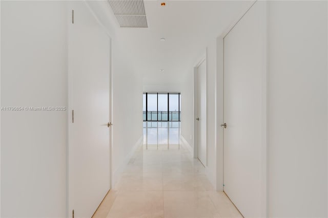 hall with light tile patterned floors, visible vents, and baseboards