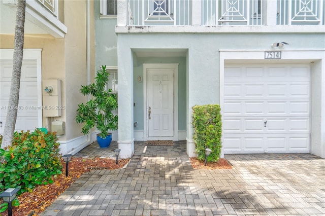 property entrance featuring stucco siding, decorative driveway, and an attached garage