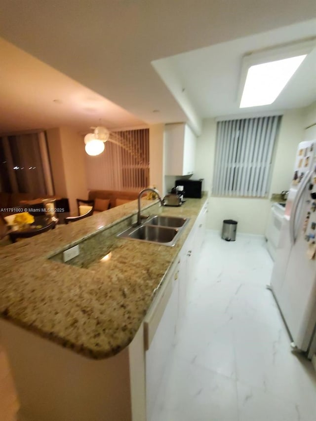 kitchen with light stone counters, a sink, white fridge with ice dispenser, marble finish floor, and a peninsula