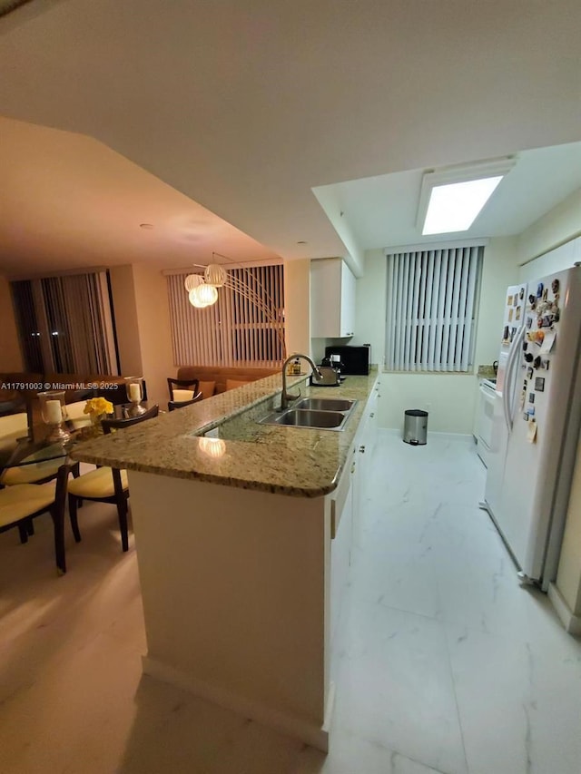 kitchen with white cabinets, light stone counters, an inviting chandelier, a sink, and freestanding refrigerator