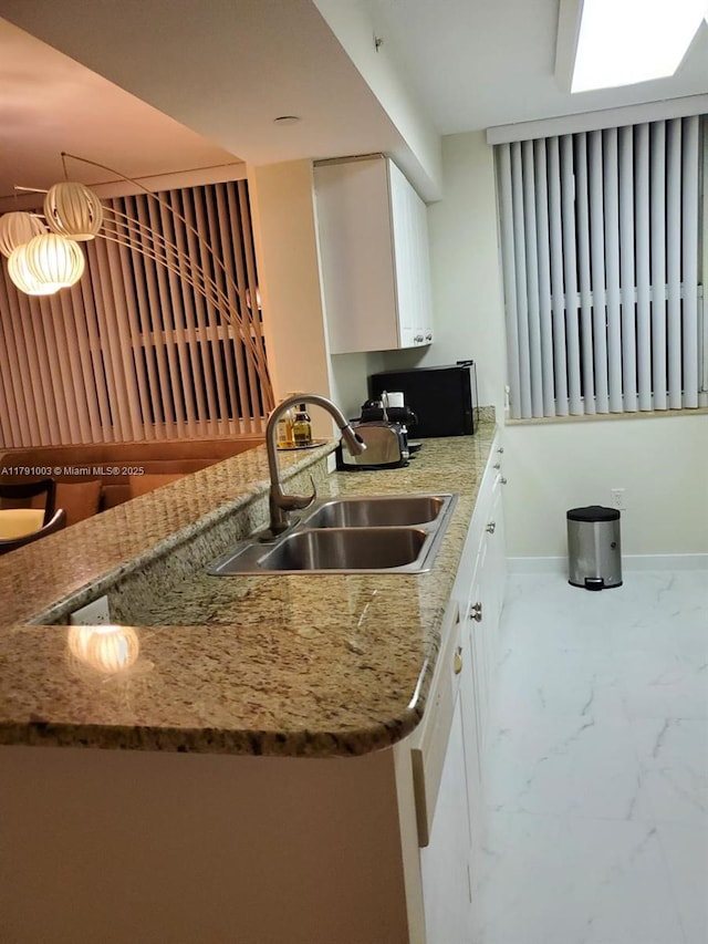 kitchen featuring marble finish floor, baseboards, white cabinets, light stone counters, and a sink