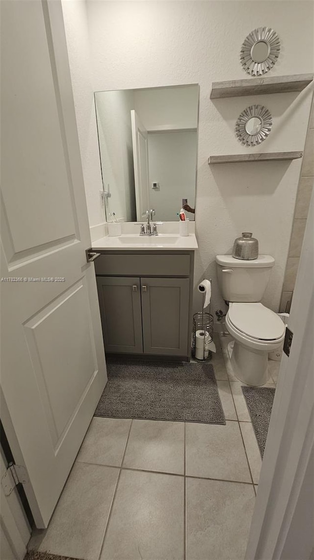 half bath featuring tile patterned floors, toilet, and vanity