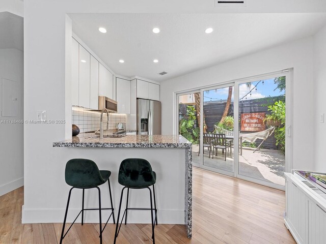 3025 SW 13th St, Miami, FL 33145 - kitchen with appliances with stainless steel finishes, a breakfast bar, white cabinetry, light stone countertops, and backsplash