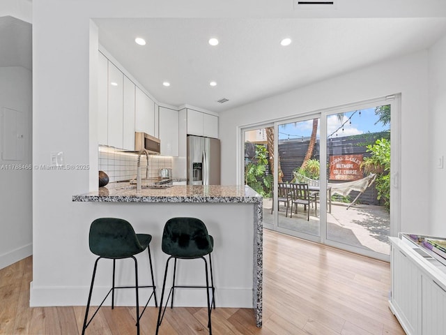 3025 SW 13th St, Miami, FL 33145 - kitchen with appliances with stainless steel finishes, a kitchen breakfast bar, white cabinetry, light stone counters, and backsplash