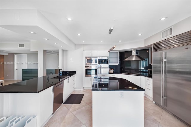 kitchen with wall chimney exhaust hood, visible vents, modern cabinets, and built in appliances