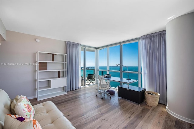 office featuring a water view, a wall of windows, wood finished floors, and baseboards