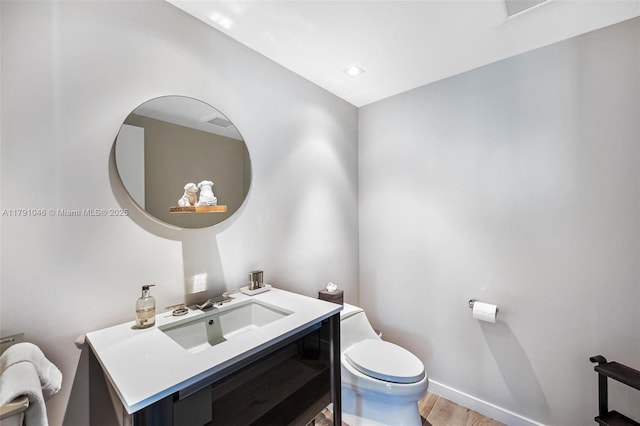 half bath featuring visible vents, baseboards, toilet, wood finished floors, and vanity