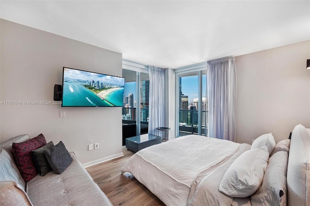 bedroom with access to outside, floor to ceiling windows, wood finished floors, and baseboards