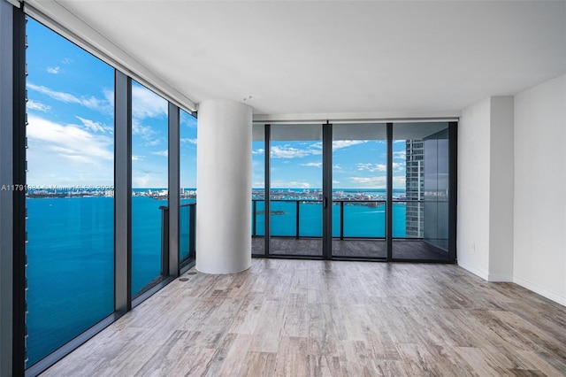 unfurnished room featuring a wall of windows, wood finished floors, a wealth of natural light, and a water view