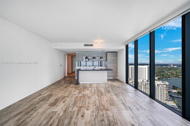 unfurnished living room featuring a wall of windows, visible vents, light wood-style flooring, and baseboards