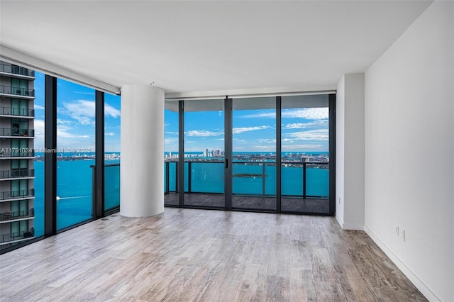 empty room featuring wood finished floors, a water view, and expansive windows