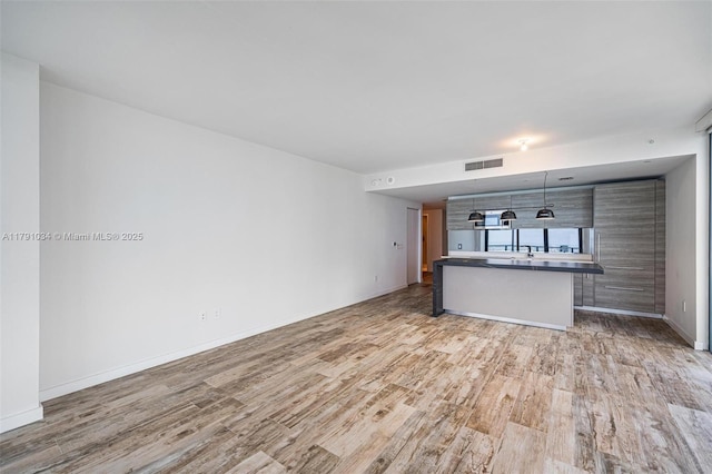 unfurnished living room with visible vents, light wood-style flooring, and baseboards