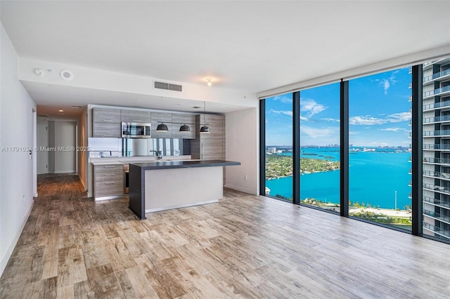 kitchen with stainless steel microwave, a water view, visible vents, a wall of windows, and wood finished floors