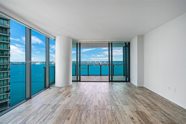 spare room featuring baseboards, wood finished floors, a water view, and expansive windows